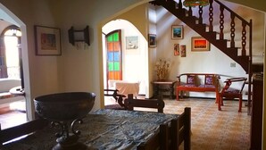 Un comedor con un recipiente metálico grande sobre una mesa, un banco de madera y una escalera que conduce a otra habitación.
