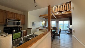 A kitchen with wooden cabinets, a microwave, and a sink. There is a staircase leading to a balcony with a view. - Enjoy the stunning ocean view from the hot tub at Port! (Southwest Harbor)