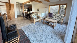 A spacious living area with a wooden ceiling, a sofa set, a coffee table, and a television on a stand. - Enjoy the stunning ocean view from the hot tub at Port! (Southwest Harbor)