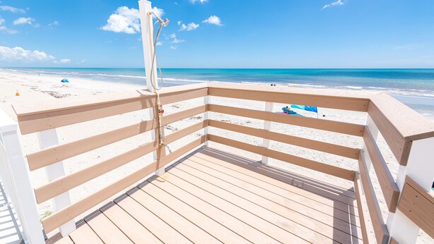 Eine Holzterrasse mit weißer Reling mit Blick auf einen Strand.