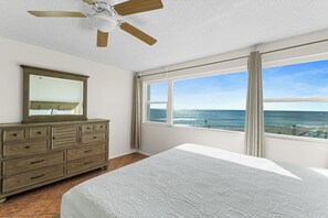 Un dormitorio con cama, cómoda, ventilador de techo y un amplio ventanal con vistas al océano.