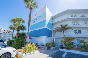 A multi-story hotel with balconies, palm trees, and a sign indicating it's the Paradise Beach Club.