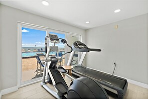 Gimnasio en casa con cinta de correr, elíptica y bicicleta estática, con vista a una piscina.