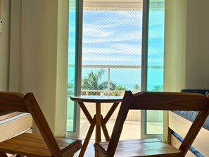 A room with a view of the ocean through large windows, a wooden table, and two wooden chairs.