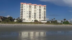 Un edificio a più piani con balconi, situato vicino a una spiaggia con acque calme.