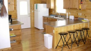 A compact kitchen with wooden cabinets, a white refrigerator, a sink, and a bar stool area.