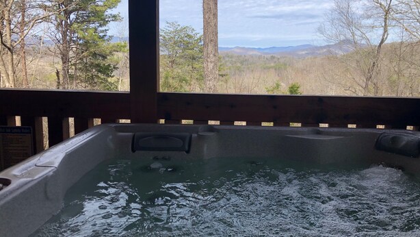 A hot tub with a wooden deck and a view of mountains and trees.