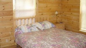A wooden cabin room with a bed, a nightstand, and a window with blinds.