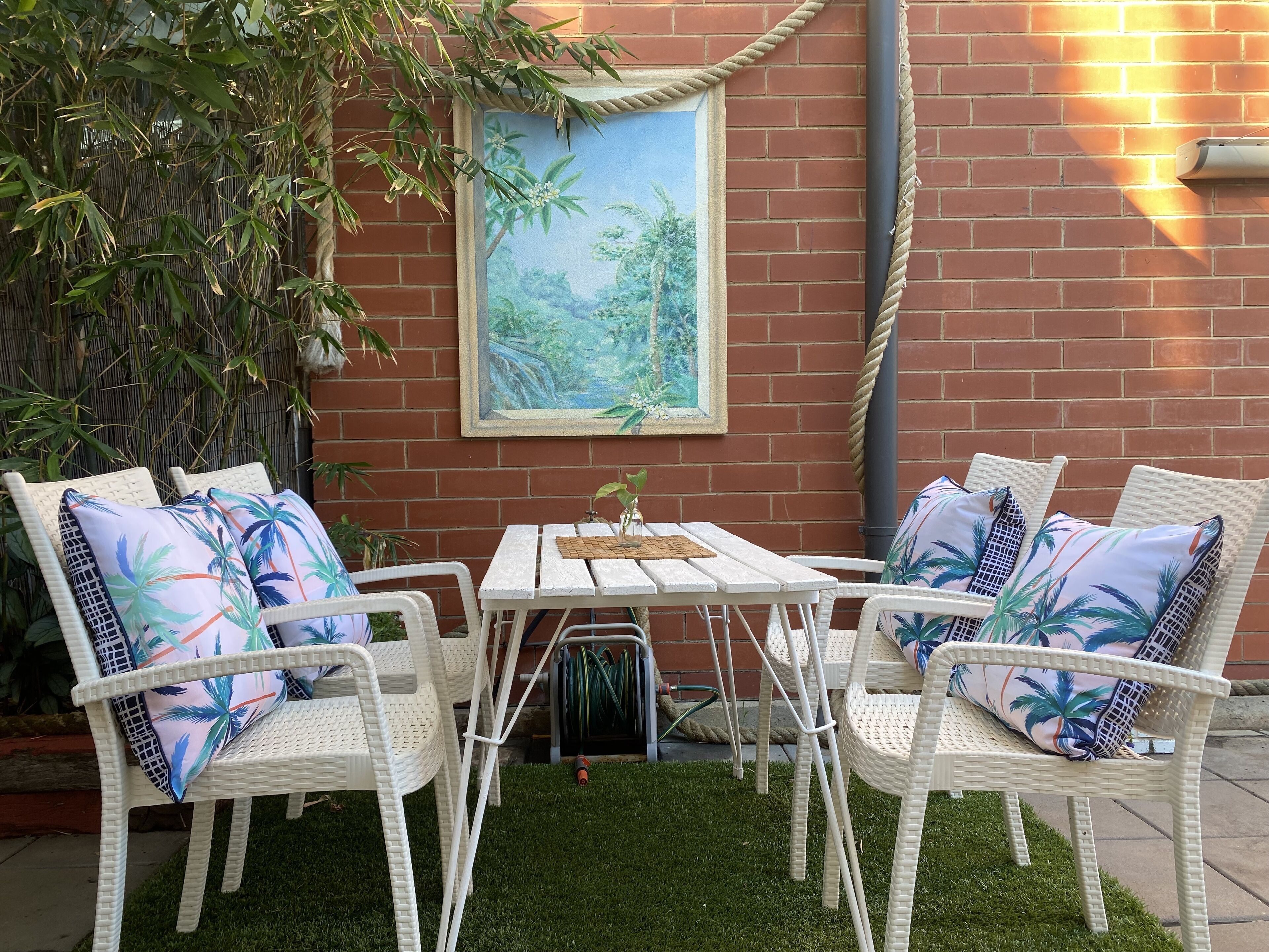 A patio with white wicker furniture, a small table, and a framed painting of a tropical scene.
