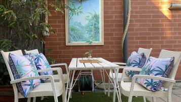 A patio with white wicker furniture, a small table, and a framed painting of a tropical scene.