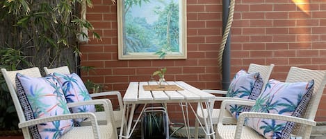 A patio with white wicker furniture, a small table, and a framed painting of a tropical scene.