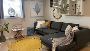 Ein Wohnzimmer mit grauem Sofa, einem gelben Teppich und einem Bücherregal mit Dekoration.