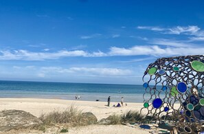 Ein Strand mit blauem Himmel, ruhiger See und einer verzierten Metallskulptur.