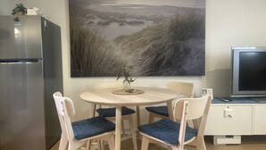 Eine kompakte Küche mit Kühlschrank, einem Esstisch mit vier Stühlen und einem großen Landschaftsbild an der Wand.