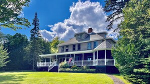 A two-story house with a covered porch and a stone pathway leading to the entrance. - HISTORIC LAKE PLACID WATERFRONT GREAT CAMP-6 BR- Each w/private full bath. (Lake Placid)