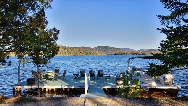 A dock with chairs and a boat, surrounded by trees and a lake. - HISTORIC LAKE PLACID WATERFRONT GREAT CAMP-6 BR- Each w/private full bath. (Lake Placid)