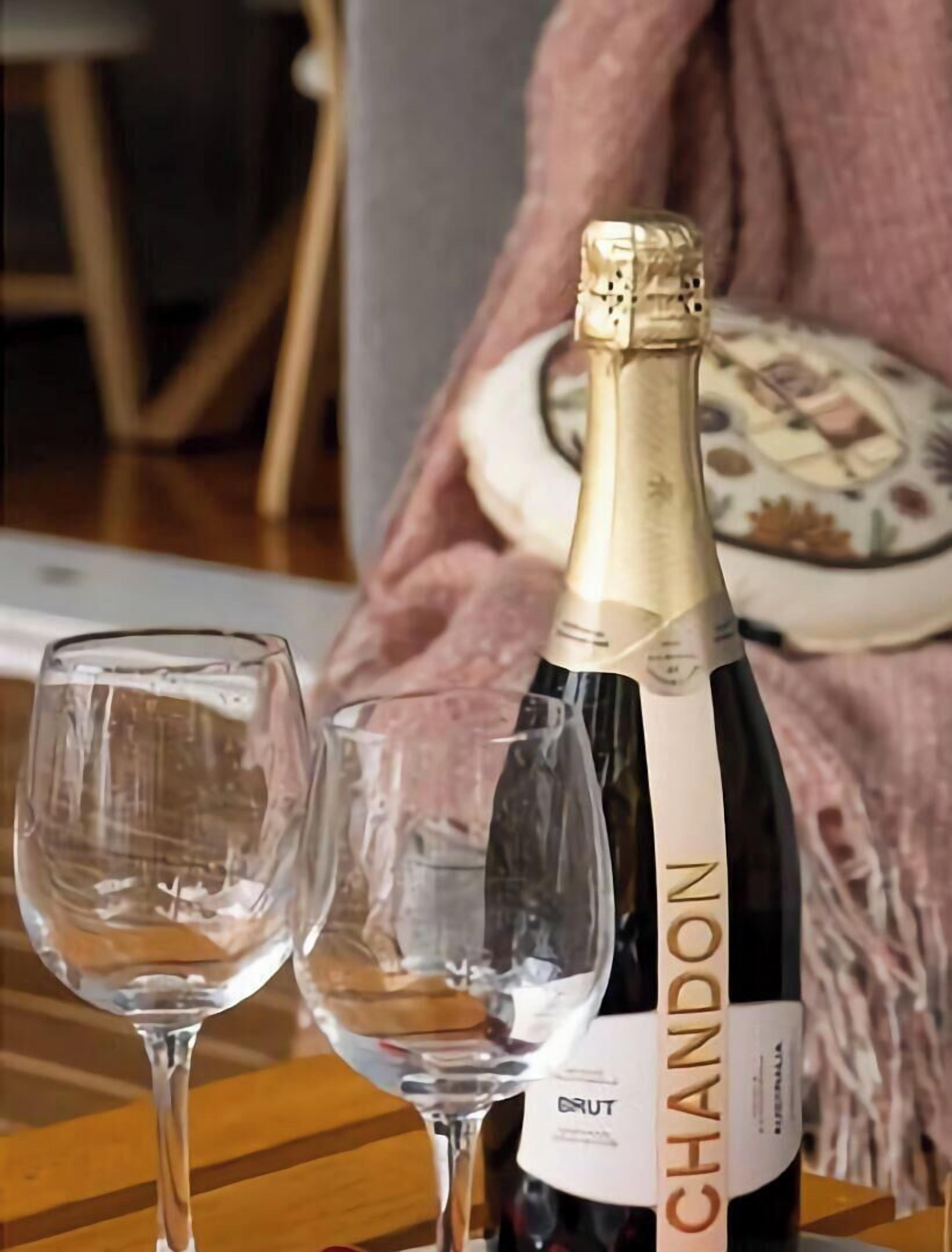 A bottle of Chandon Brut champagne and two empty wine glasses on a wooden table.