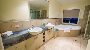 A modern bathroom with two sinks, a large bathtub, and a mirror.