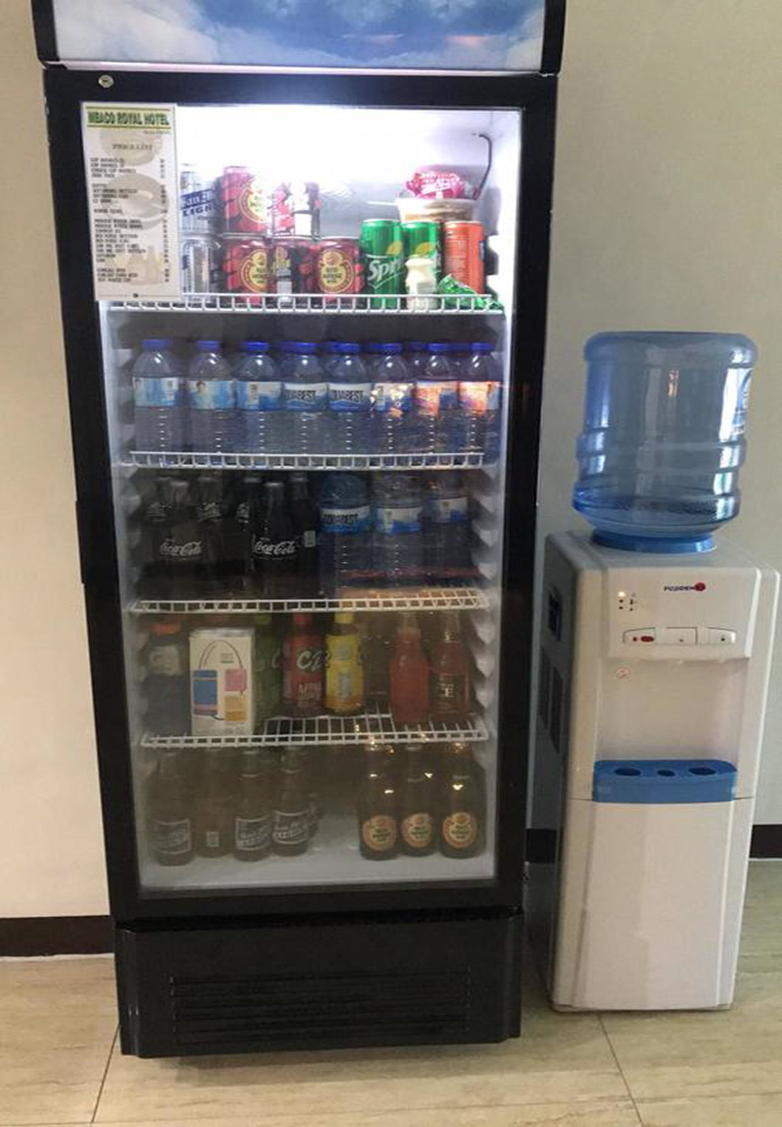 Máquina expendedora con diversas bebidas y aperitivos, incluyendo Coca-Cola y Sprite, y un dispensador de agua al lado.