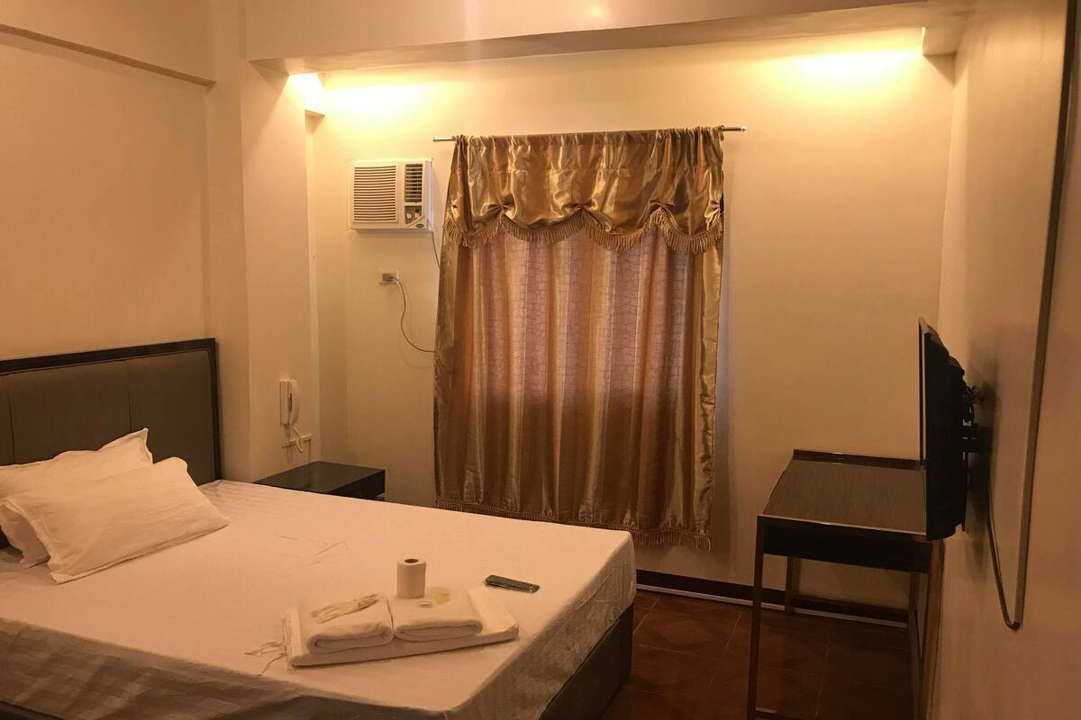 Une chambre d’hôtel avec un lit, une table de chevet, une télévision et un rideau.