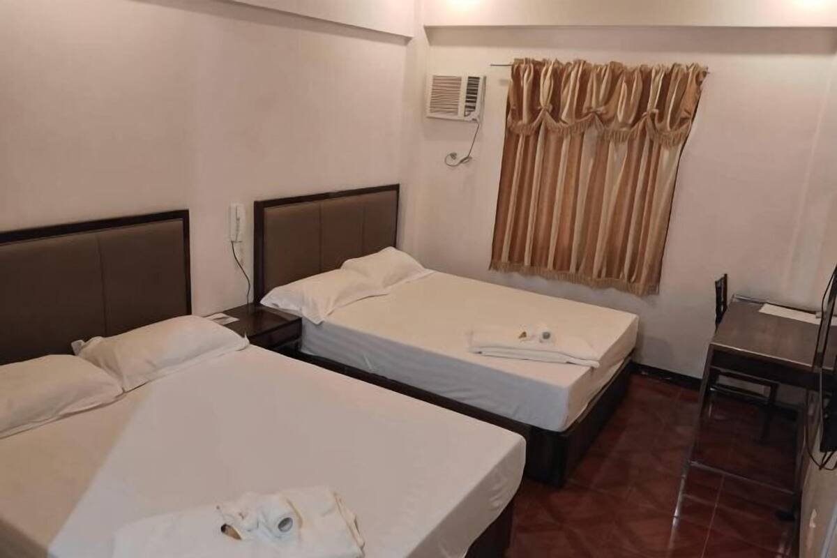 A hotel room with two beds, a chair, a desk, and a window with curtains.