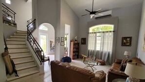 Un salon spacieux avec un escalier, un canapé en cuir marron, une table basse en verre et un ventilateur de plafond.
