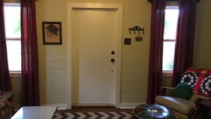 A room with a white door, a framed picture on the wall, a small sign above the door, and a patterned rug. - Peaceful, Private Cottage On Bayou Teche (New Iberia)