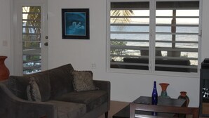 A living room with a couch, a table with decorative vases, a framed picture on the wall, and a window with a view of the ocean. - Sea Breeze - FABULOUS NORTH SHORE (Vieques)