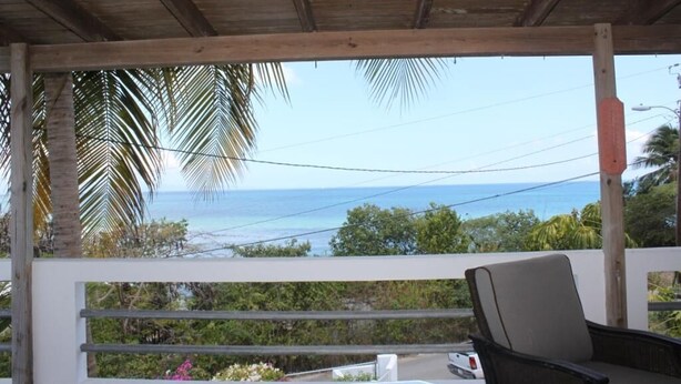 A covered outdoor area with a view of the ocean, a chair, and a white vehicle. - Sea Breeze - FABULOUS NORTH SHORE (Vieques)