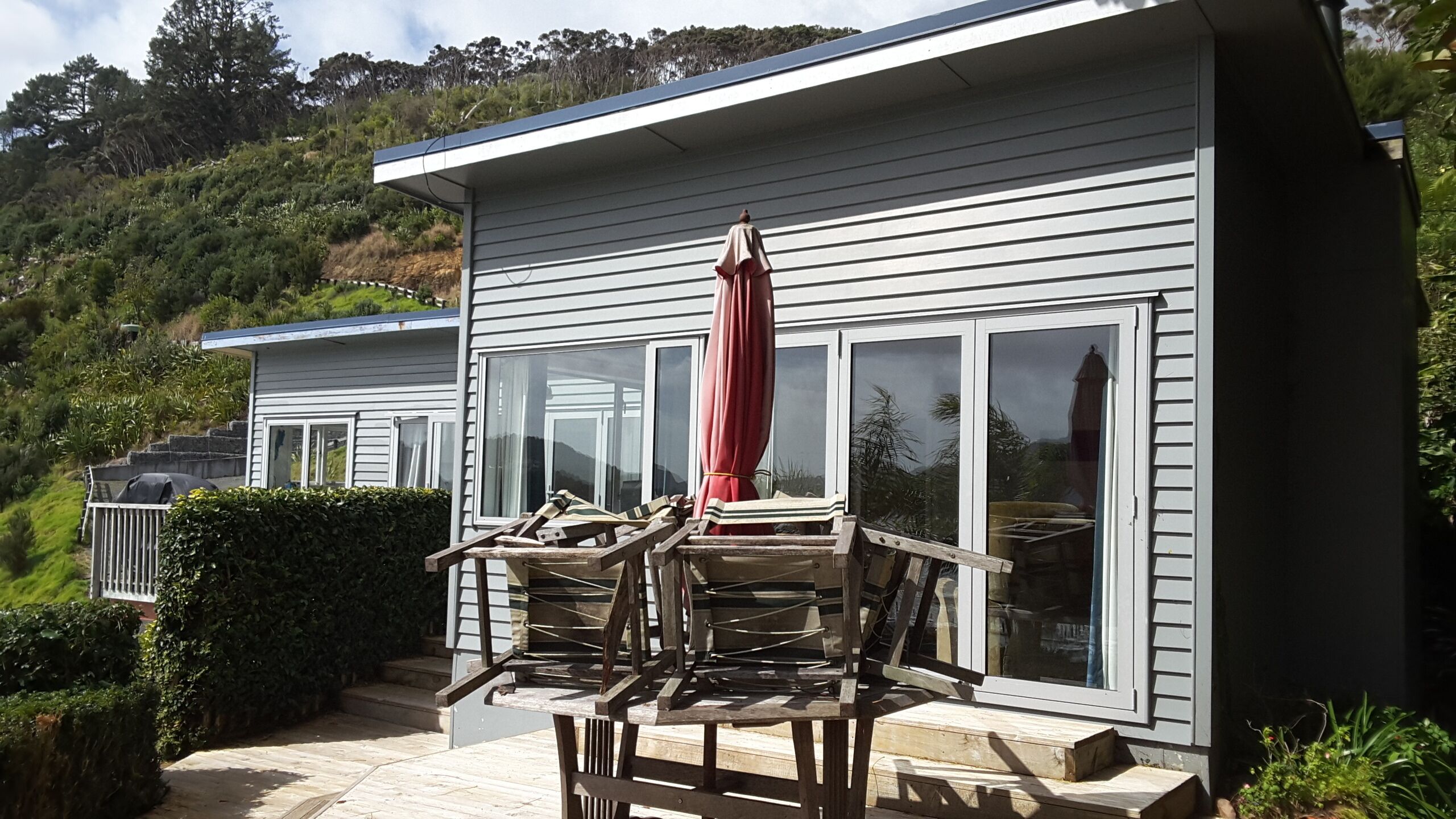 Une maison moderne dotée d’un patio comprenant une table en bois et un parasol rouge.