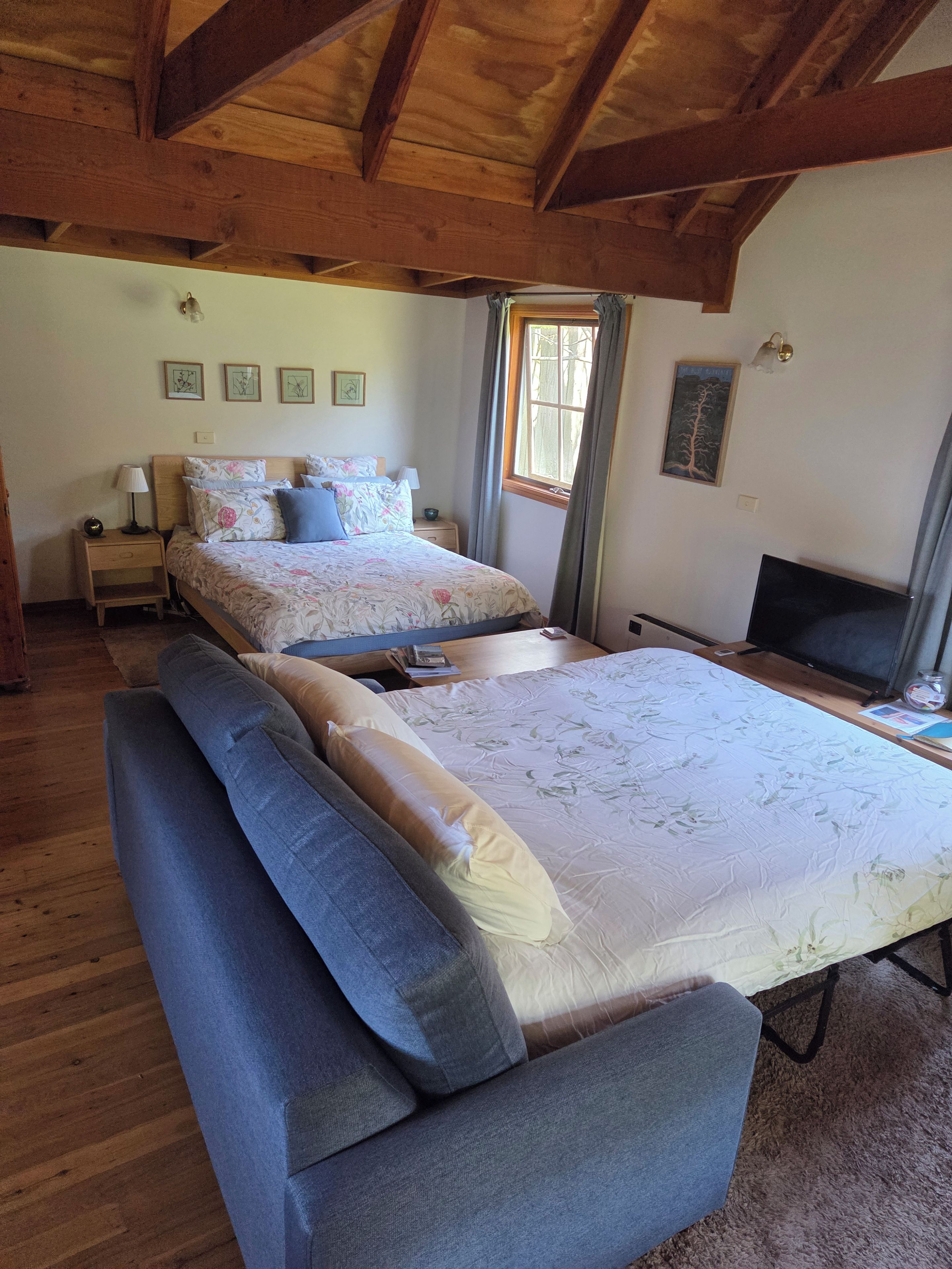 Une chambre avec un grand lit, un plus petit lit, un canapé, une télévision et des poutres en bois au plafond.