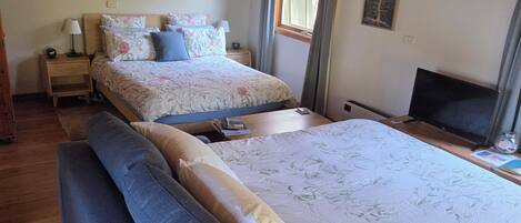 Une chambre avec un grand lit, un plus petit lit, un canapé, une télévision et des poutres en bois au plafond.