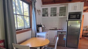 A kitchen with white cabinets, a stainless steel refrigerator, a coffee maker, and a dining table with chairs.