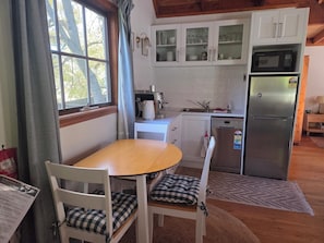 A kitchen with white cabinets, a stainless steel refrigerator, a coffee maker, and a dining table with chairs.