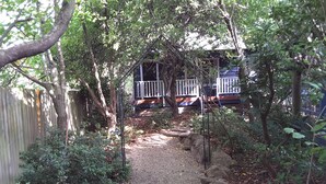 A gravel path leading to a wooden deck with a white railing, surrounded by dense foliage and a wooden fence.