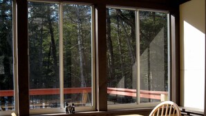 Ein Zimmer mit einem großen Fenster, einem Holztisch und zwei Holzstühlen.