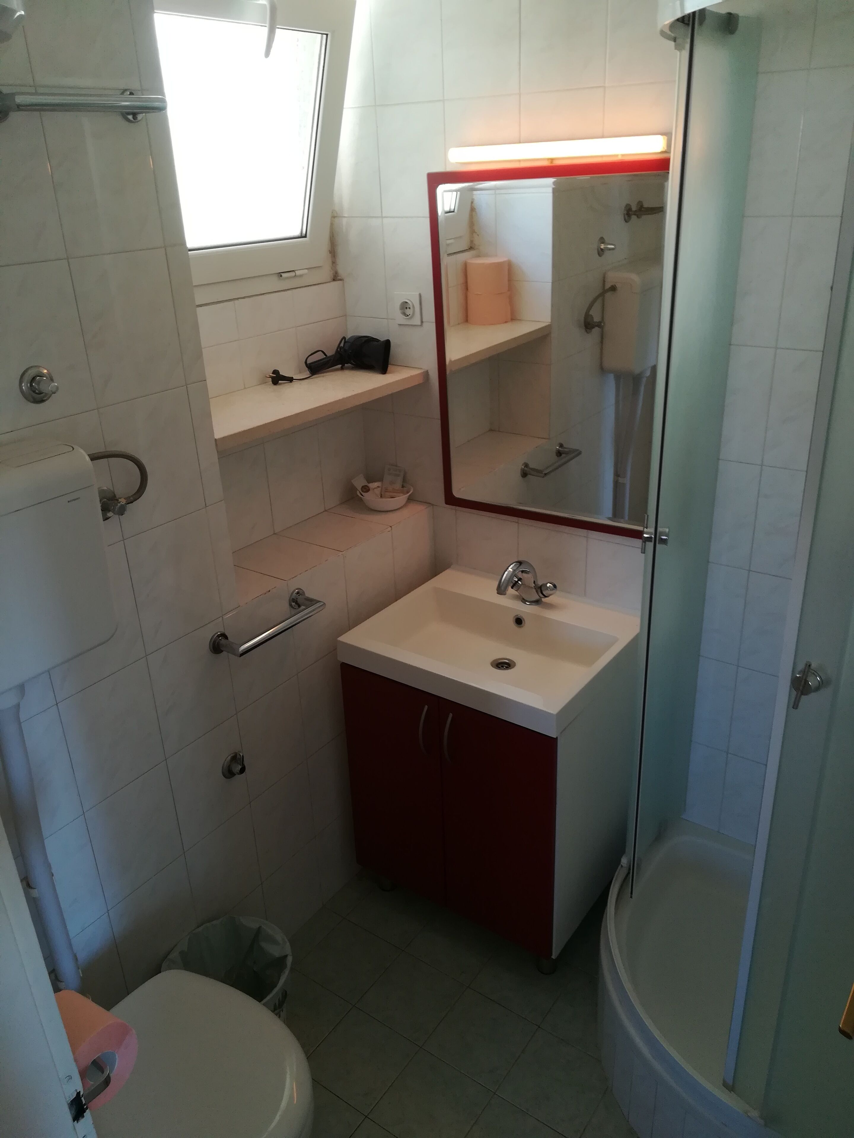 A compact bathroom with a white sink, a mirror, a shower, and a toilet.