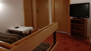 Um quarto com uma cama, uma mesinha, uma televisão sobre um suporte e três portas de madeira.