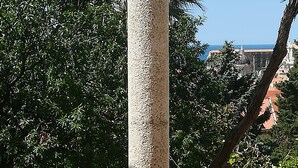 Um pilar de pedra com uma placa, rodeado por vegetação exuberante e rosas cor-de-rosa.