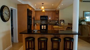 Una cocina con armarios de madera, una isla central con taburetes, un reloj y un microondas.
