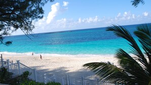 Una playa con agua turquesa cristalina, arena blanca y algunas personas caminando.