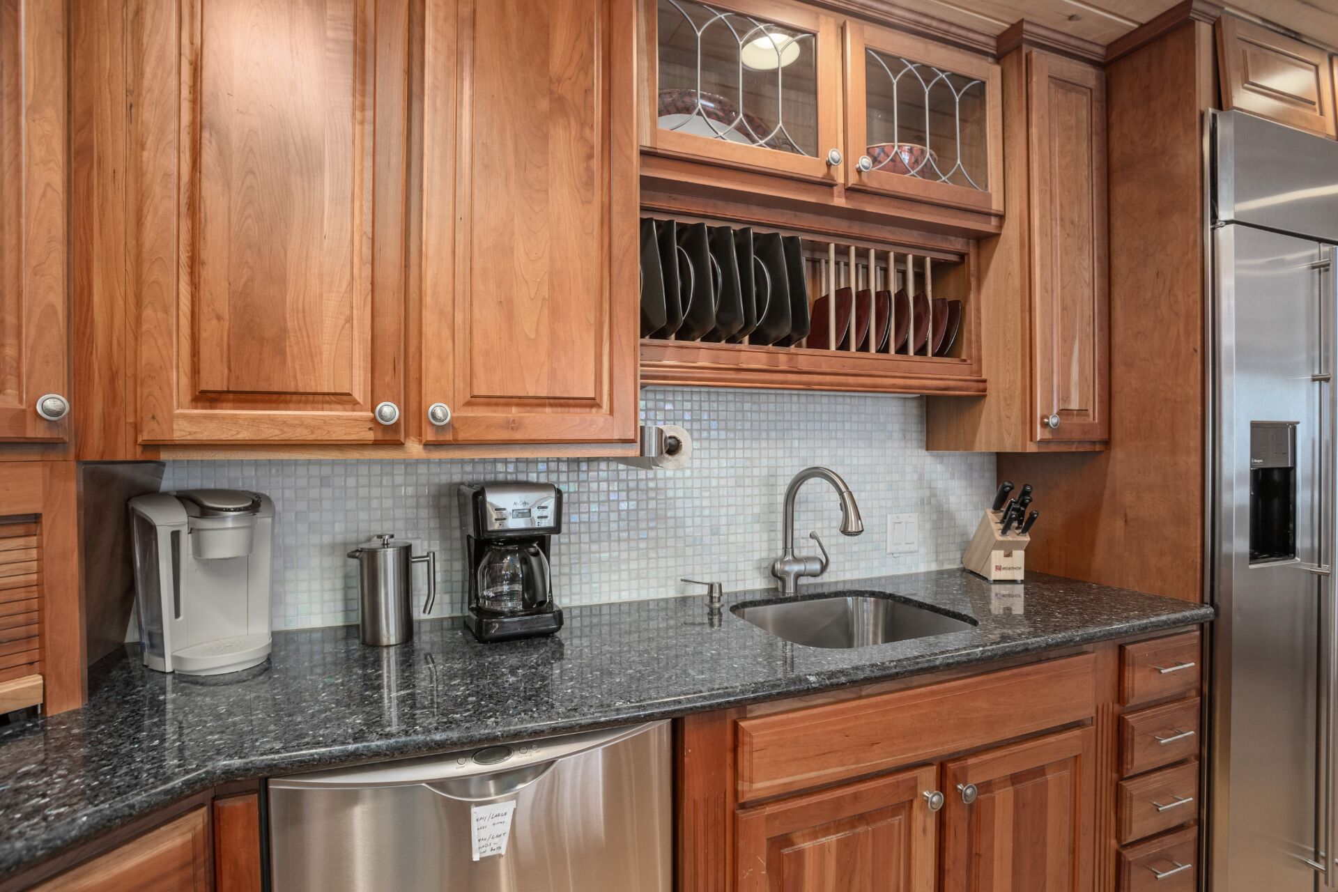 Una cocina con armarios de madera, un refrigerador de acero inoxidable, una cafetera y un lavamanos.