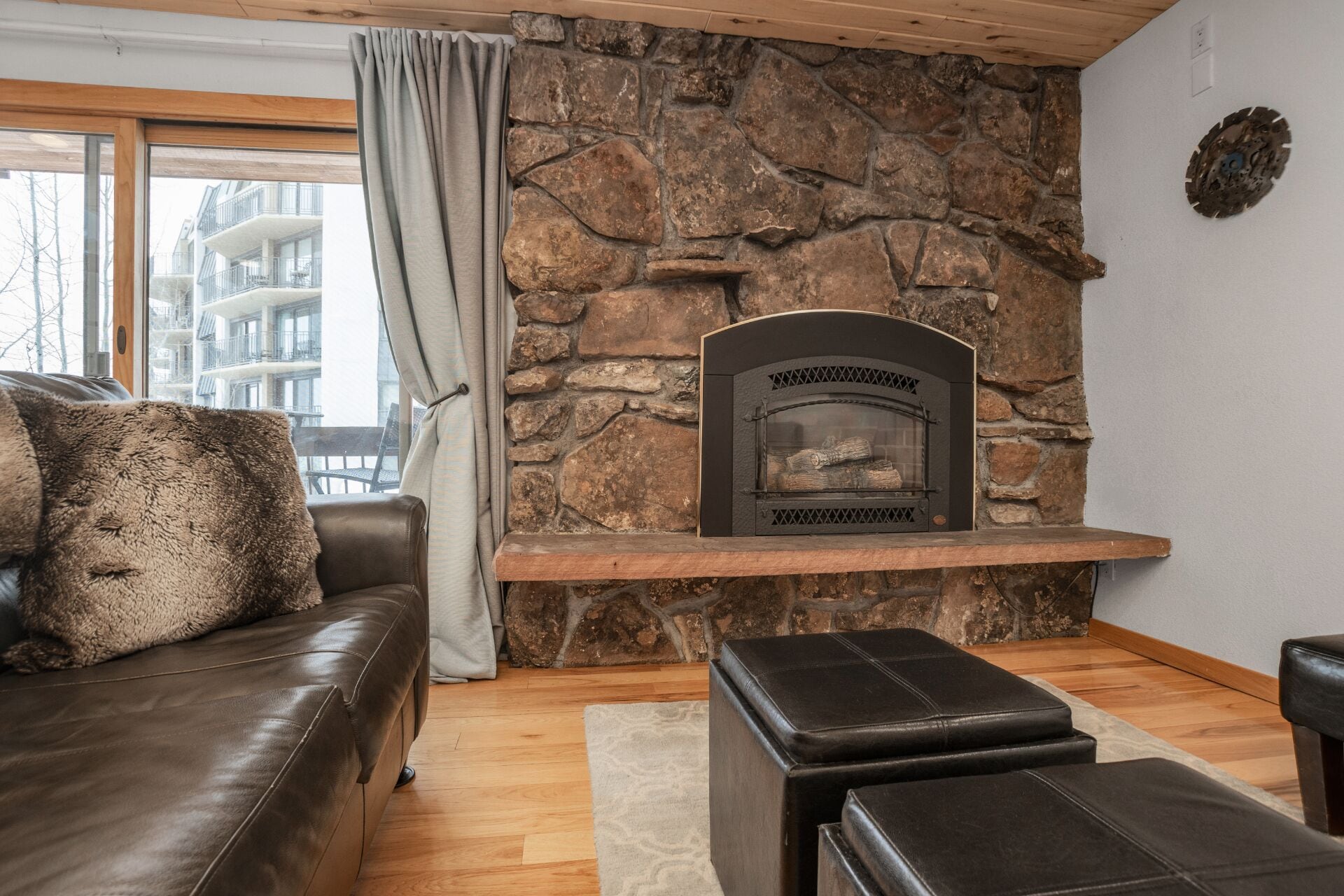 Una sala de estar con pared de piedra, chimenea, sofá de cuero y ventana con cortinas.