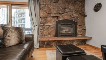 Una sala de estar con pared de piedra, chimenea, sofá de cuero y ventana con cortinas.