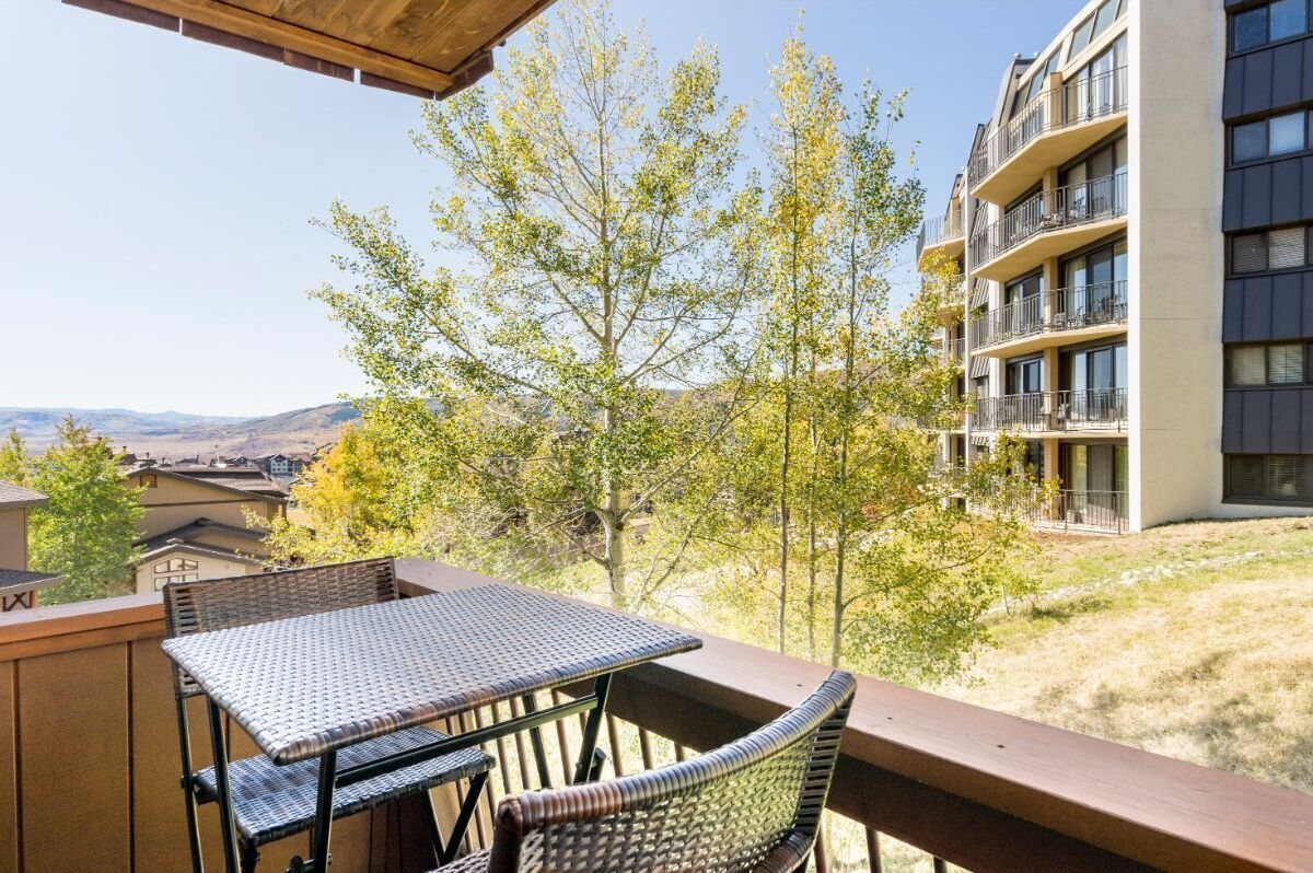 A balcony with wicker furniture, a view of trees, and a building in the background.