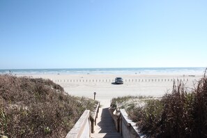 Ein Strandweg führt zum Ufer, wo ein Auto am Strand geparkt ist.