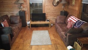 Un accogliente soggiorno con pareti in legno, una TV a schermo piatto, due divani in pelle, un tavolino da caffè e un tappeto.