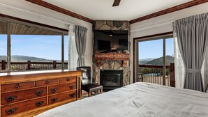 Un dormitorio con una cama grande, un aparador, una chimenea de piedra y vistas a las montañas.