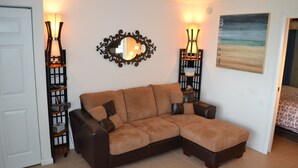 A corner living room with a brown leather sofa, a decorative mirror, two wall-mounted lamps, and a beach-themed painting. - Oceanfront!!! Clean and Cozy, Free Wi-Fi & calls to US and Canada (Lauderdale-by-the-Sea)