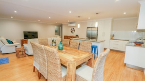 A modern kitchen with white cabinets, a stainless steel refrigerator, and a dining area with wicker chairs and a wooden table.